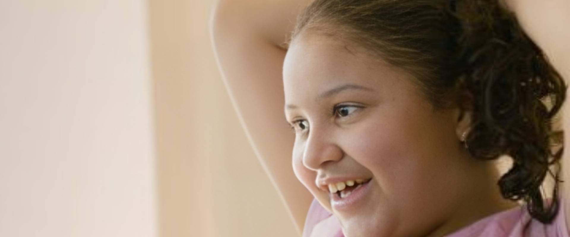 A young girl smiling with her hand up to the side.