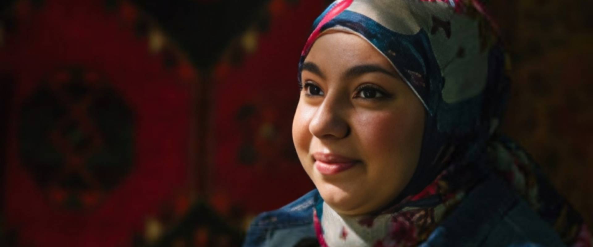 A woman wearing a head scarf and smiling.